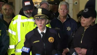 Superintendent Anne Kirkpatrick flanked by several police officers speaking into press microphones