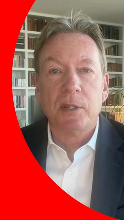 Frank Gardner, with short hair, dressed in a suit in front of a bookcase.
