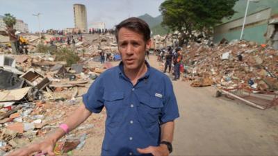 Man in blue shirt walking among rubble after earthquake