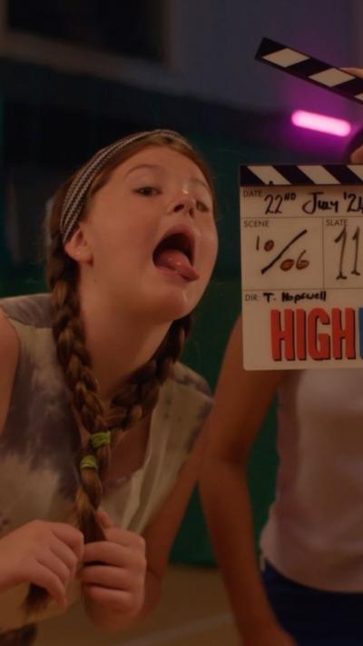 A young girl is sticking her tongue out next to a clapper board