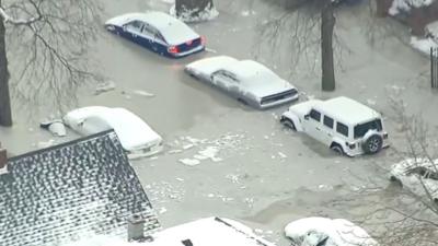 Cars in a street are half-submerged in snow covered water.