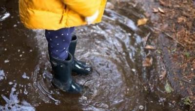 A child wearing wellington boots and a yellow rain coat standing in a puddle.