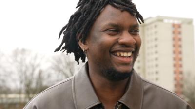 Musician Victor Ray smiling at camera and wearing a brown jacket