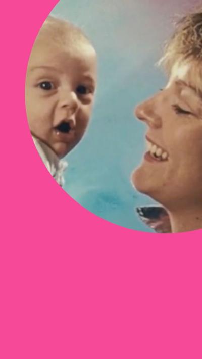 Side view of a woman smiling holding up a young baby,