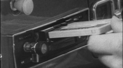 A hand places a casette tape into a car's tape player.