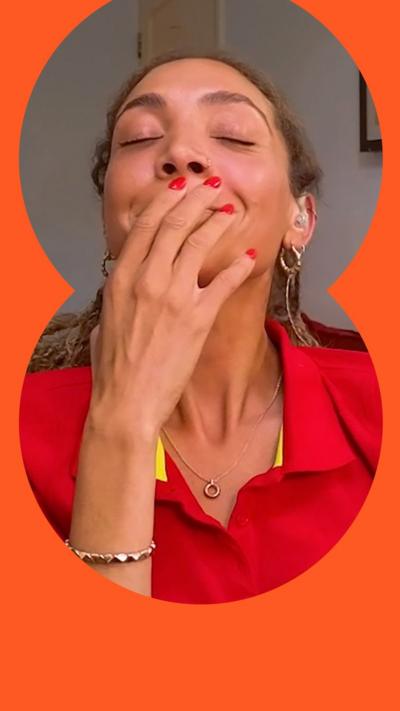 Miquita Oliver covers her mouth as she smiles with her eyes closed. She wears a red shirt and her hair is tied back.