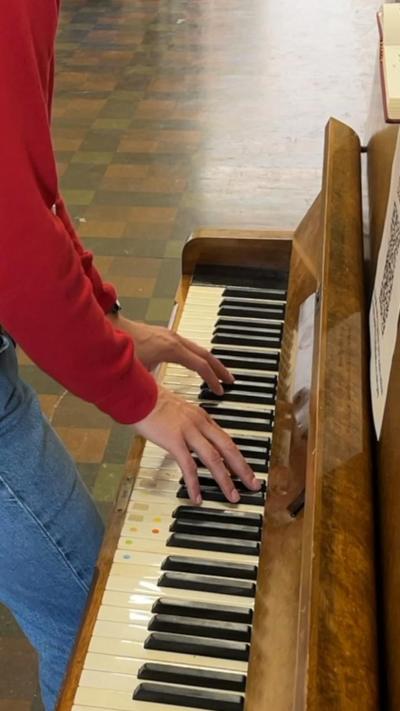 A close-up of piano keys. A man's hands and arms are also in the picture. They are wearing a red top and jeans. 