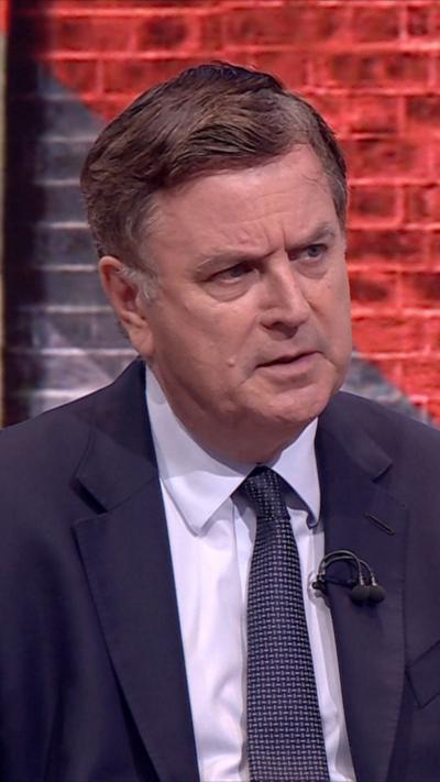 Mel Stride has short greying hair and wears a suit and tie in the studio