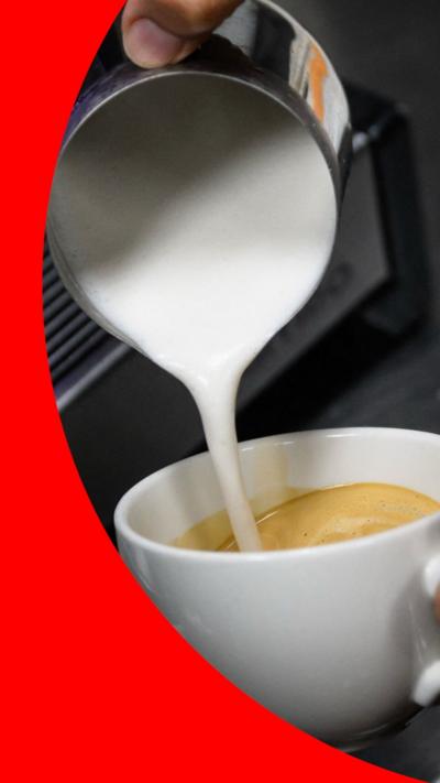Milk being poured from a silver jug into a cup of coffee