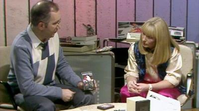 Lesley Judd and John Coll sit at a table, surrounded by technological gifts