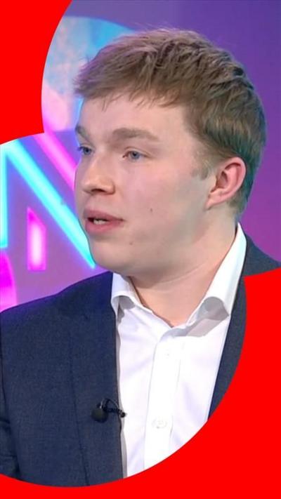 A man wearing a white shirt and suit jacket sitting in front of a purple background