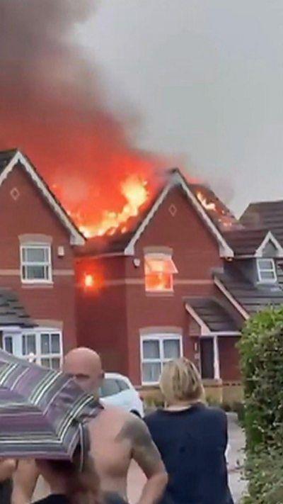 People standing in front of a house that is on fire.