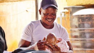 A man holding a toy baby and smiling