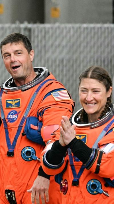 Astronauts wearing orange space suits smile and clap while acknowledging a crowd of well-wishers