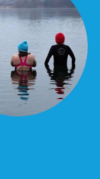 Two people wearing swimming costumes and beanie hats stand in a lake