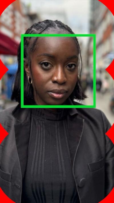 A woman in a black jacket stands in the street. A green box outline highlights her face