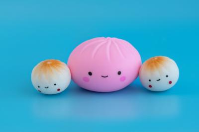 3 squishy fidget toys that look like dumplings with smiley faces appear on a blue background