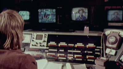 Man sits at control panel with four tv screens