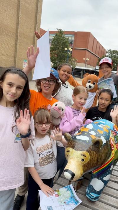 A group of children wave beside a colourful painted bear sculpture while holding trail maps in Scunthorpe town centre as part of the We're Going on a Bear Hunt art trail.