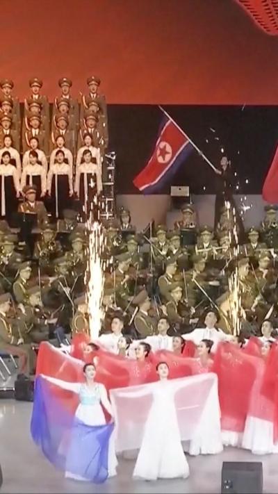 A stage filled with performers dressed in white holding red and blue material with a band in the background.