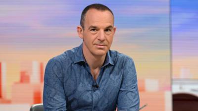 Martin Lewis wearing a blue shirt in front of a blue and orange background