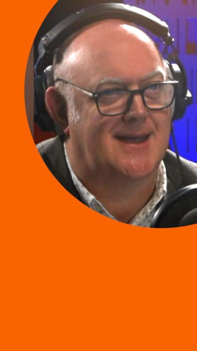 Dara Ó Briain wears glasses and headphones in a radio studio