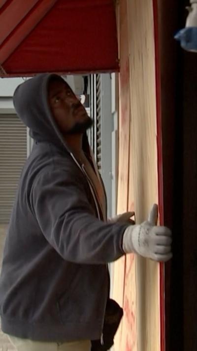 A man wearing a hooded jumper and gloves lifts a wooden panel onto a door
