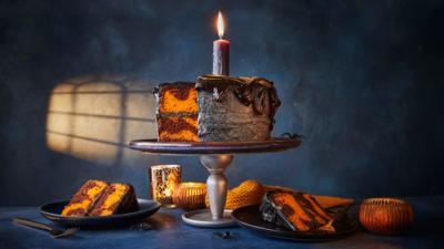 A chocolate marble cake on a black stand with a candle on the top.