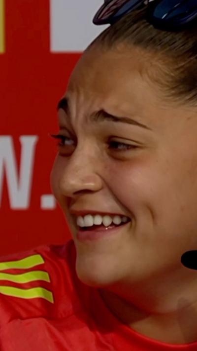 A woman in a red Wales shirt laughing. She has sunglasses on her head. 