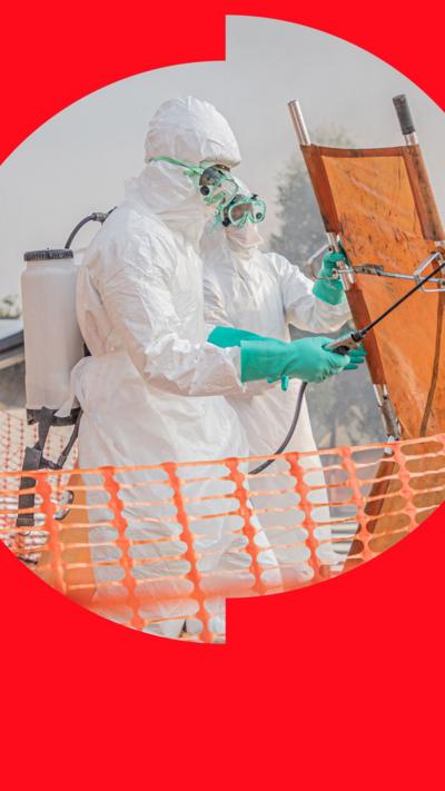 Two medical workers in protective clothing spraying down an orange stretcher amid Ebola outbreak. 