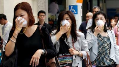 Women cover their faces with masks as haze shrouds Singapore"s central business district.