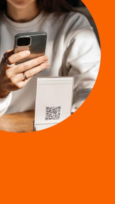 A woman sat at a restaurant table scanning a QR code with her phone.There is a salt and pepper shaker and a half eaten plate of food next to her on the table