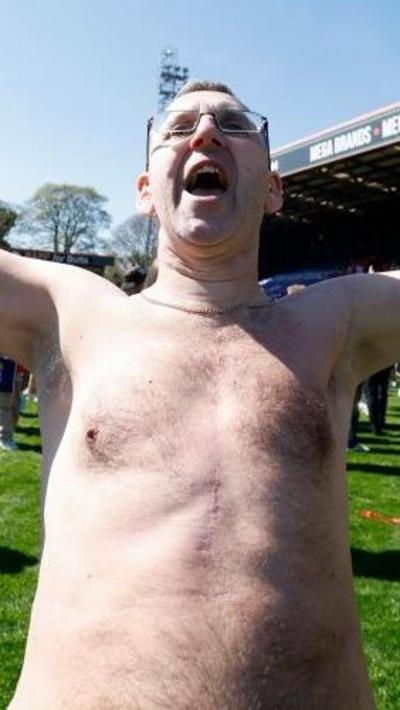 Man with top off celebrates winning a football match