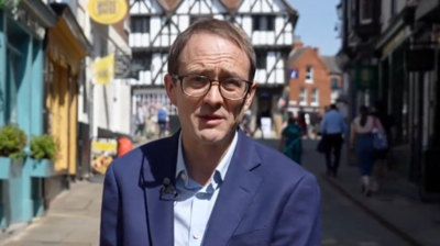 Chris Mason on a town centre street - he wears a blue suit and brown glasses