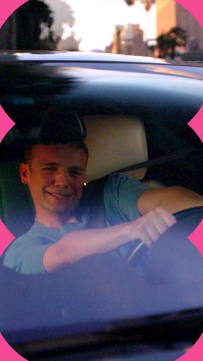 Alasdair Keane sits behind the wheel of a car, appearing to swerve