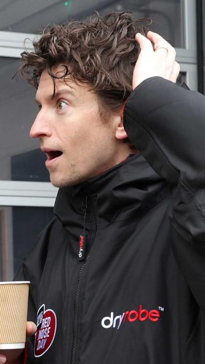 Greg James holding a coffee cup and looking shocked.