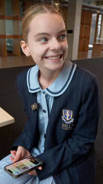 Teen girl wearing scchool uniform smiles over her shoulder while holding phone