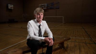 Sport student Loui sits on a wooden bench in the school sports hall