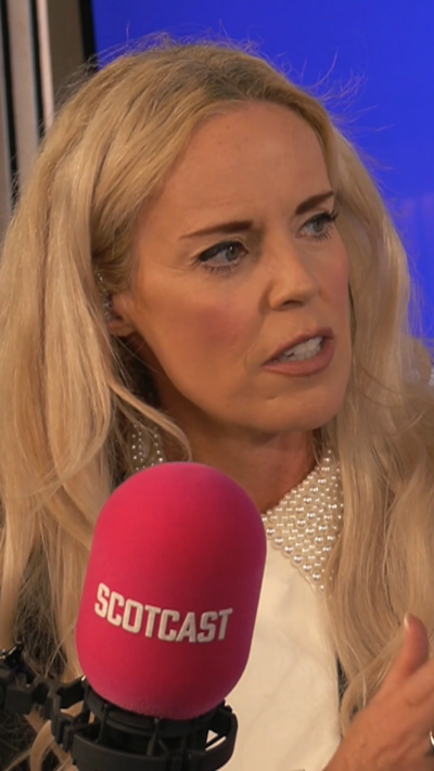 A woman with long, blonde hair and a white top in front of a red microphone with Scotcast written on it.