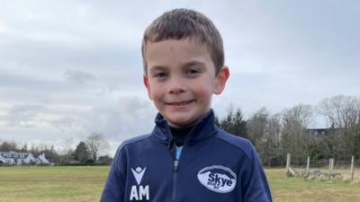 Archie na sheasamh air pàirce agus gàire mhòr air aodann. 