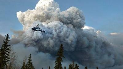 A helicopter flies close to a huge cloud of smoke from wildfires in Fort McMurray in Alberta, Canada.