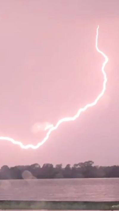 Image of a large arc of lightning streaking across the sky. The bolt is bright enough to tinge the sky a reddish pink.