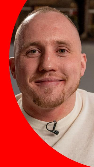 A man smiles at the camera, he has close-cropped hair and a short beard
