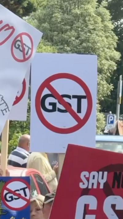 A white placard with black text reading 'GST' with a red cross through the middle
