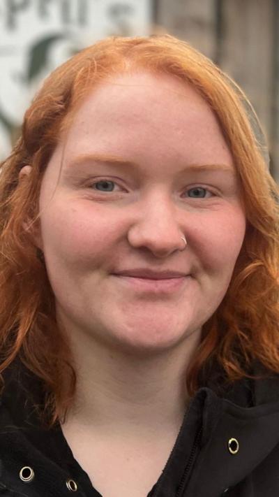 Emily smiles at the camera. She has ginger short curly hair and wears a collared, black waterproof jacket.