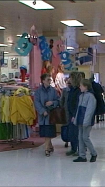 Two women and a boy walk through a shopping centre in the 1980s.