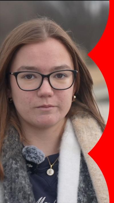 A young woman with glasses and long brown hair looks at the camera