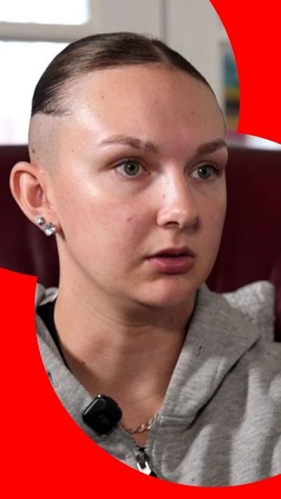 A young woman with a short skin fade and her hair scraped back from her face looks at someone off-camera