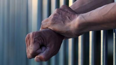 Prisoner hanging arms outside prison bars