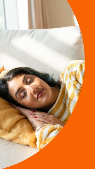 A woman naps. She has black hair and a yellow and white striped top. Sun streams in the window.